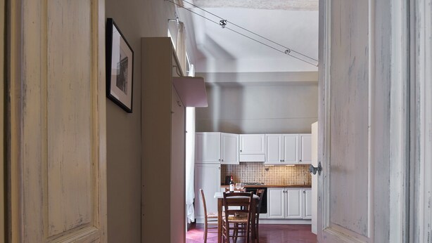 A narrow hallway leading to a kitchen with white cabinets and a tiled backsplash. - Pergola One Romantic Apt by Oteego (Florence)