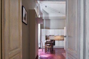 A narrow hallway leading to a kitchen with white cabinets and a tiled backsplash.