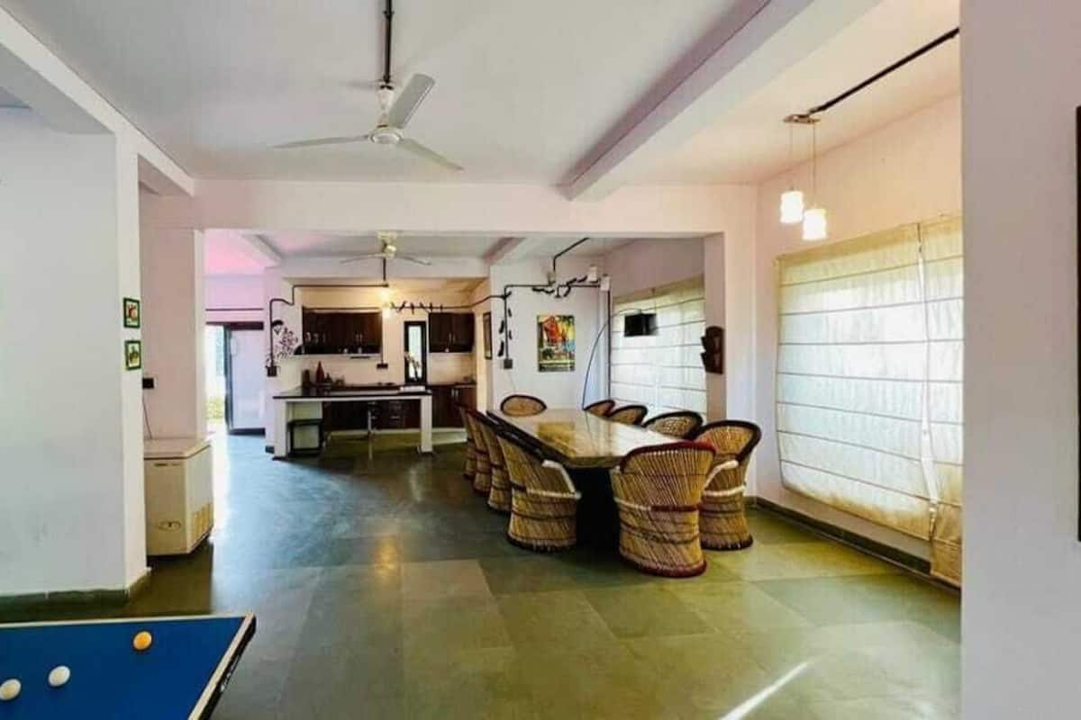 A spacious dining area with a long table and wicker chairs, a ceiling fan, and a kitchen in the background.