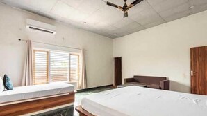 A hotel room with two beds, a wooden headboard, a ceiling fan, and a window with blinds. - Evergreen Resort & Farm Aravali (Gurugram)