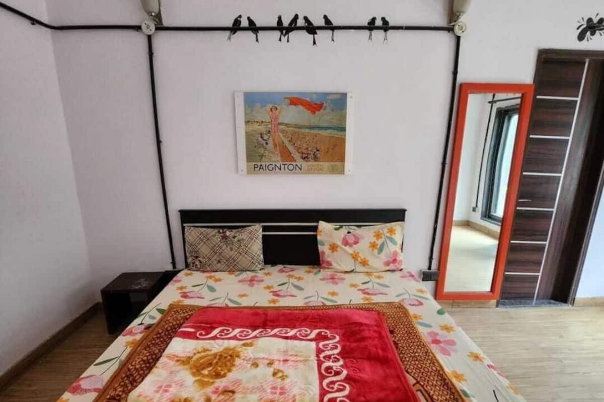 A bedroom with a bed, a nightstand, a wall-mounted lamp, a painting, and a mirror.