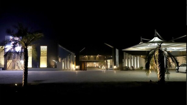 Un bâtiment moderne doté d’une façade en verre, de palmiers et d’un espace extérieur couvert.