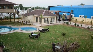 Un jardin avec une piscine, une terrasse couverte et une pelouse.