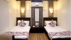 Une chambre d’hôtel avec deux lits, chacun recouvert d’une couvre-lit à motifs floraux, une table de chevet avec une bouteille d’eau et un climatiseur fixé au mur.