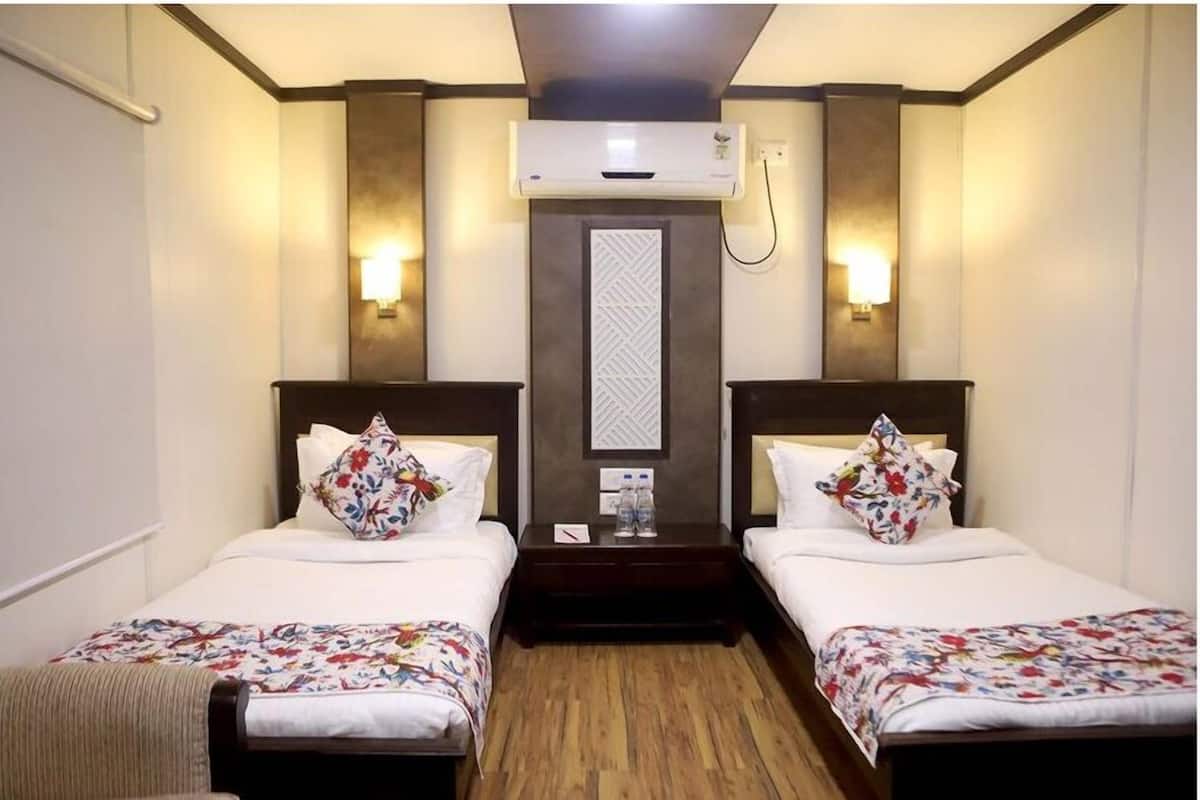 Habitación de hotel con dos camas, cada una con cubrecama floral, una mesita de noche con una botella de agua y un aire acondicionado de pared.