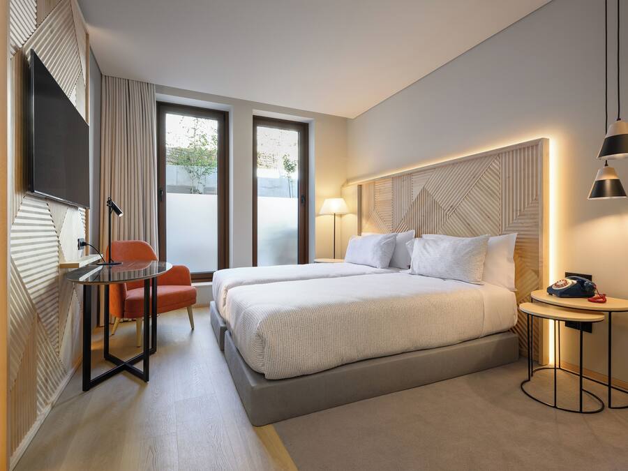Ein modernes Hotelzimmer mit einem großen Bett, einem Schreibtisch mit Stuhl, einem Fernseher und einem kleinen Tisch mit Lampe.