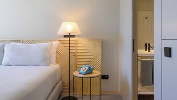 Hotelkamer met een bed, een bedlampje, een klein tafeltje met een telefoon en een badkamer zichtbaar door een open deur.