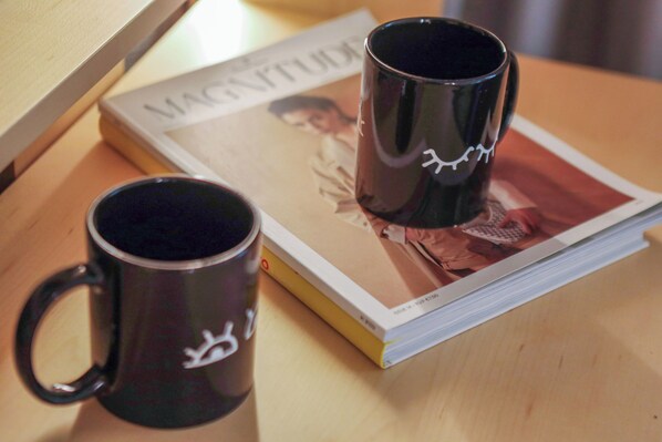 Two black mugs with white designs on a wooden table, next to a magazine with a visible image of a person. - INNSiDE By Meliá Braga Centro (Braga)