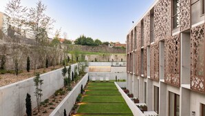 A modern building with a central courtyard featuring a neatly trimmed lawn, seating areas, and decorative lighting. - INNSiDE By Meliá Braga Centro (Braga)