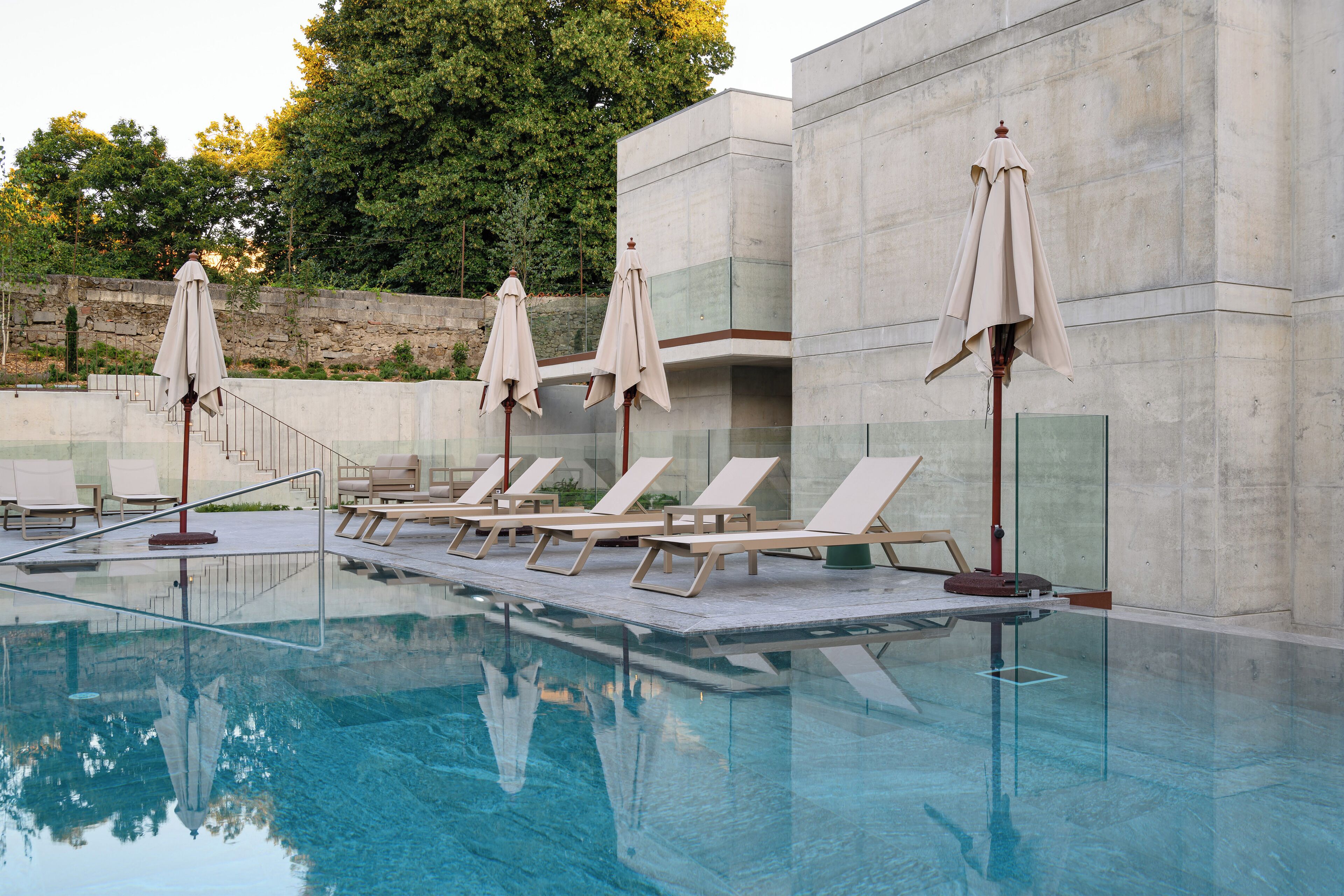 A swimming pool with lounge chairs and umbrellas, surrounded by a stone wall and trees.