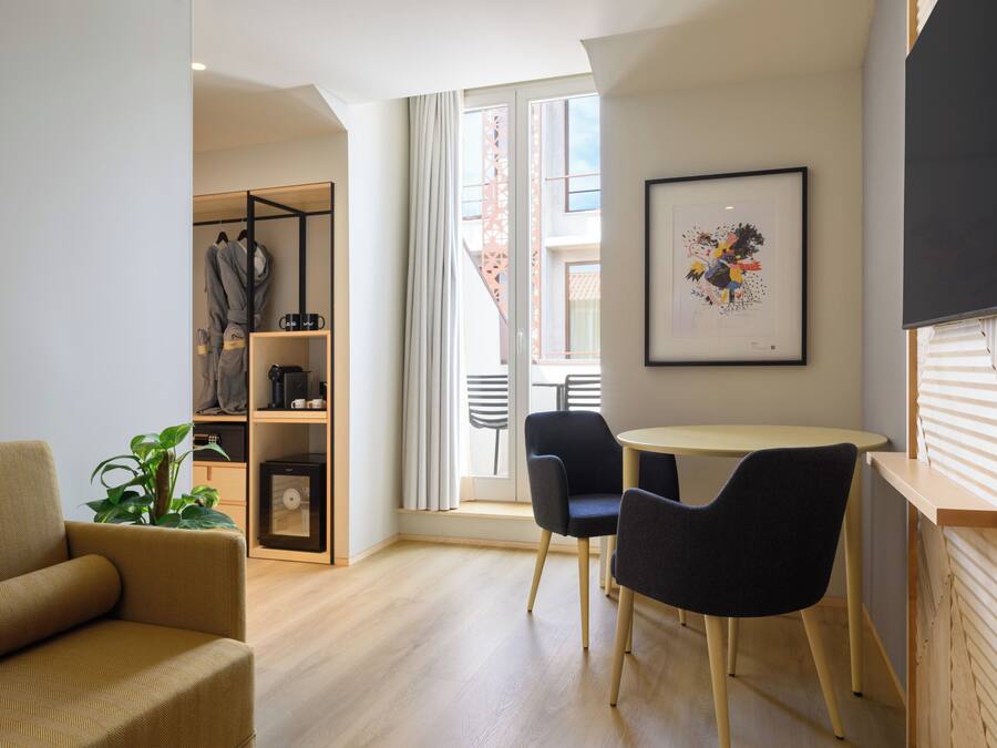 Ein modernes Wohnzimmer mit einer Couch, einem Esstisch mit Stühlen, einem Bücherregal und einem großen Fenster mit Vorhängen.