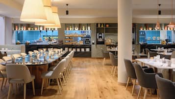 Un restaurante moderno con una mesa común alargada, mesas para comensales individuales y una zona de cocina visible al fondo.