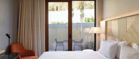 Habitación de hotel con dos camas, un escritorio, una silla naranja, una lámpara y vistas a través de un ventanal.