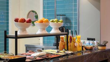 A buffet with various food items and beverages, including bowls of fruits and a selection of drinks.