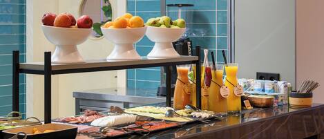 A buffet with various food items and beverages, including bowls of fruits and a selection of drinks.