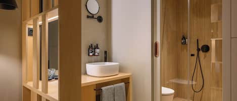 Un baño moderno con tocador de madera, espejo redondo, lavabo blanco y zona de ducha con mampara de vidrio.