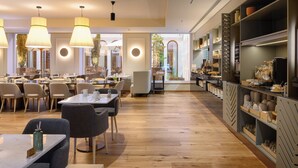 A modern restaurant with wooden floors, round tables, and chairs. There are pendant lights hanging from the ceiling and a large window with a view of greenery. - INNSiDE By Meliá Braga Centro (Braga)