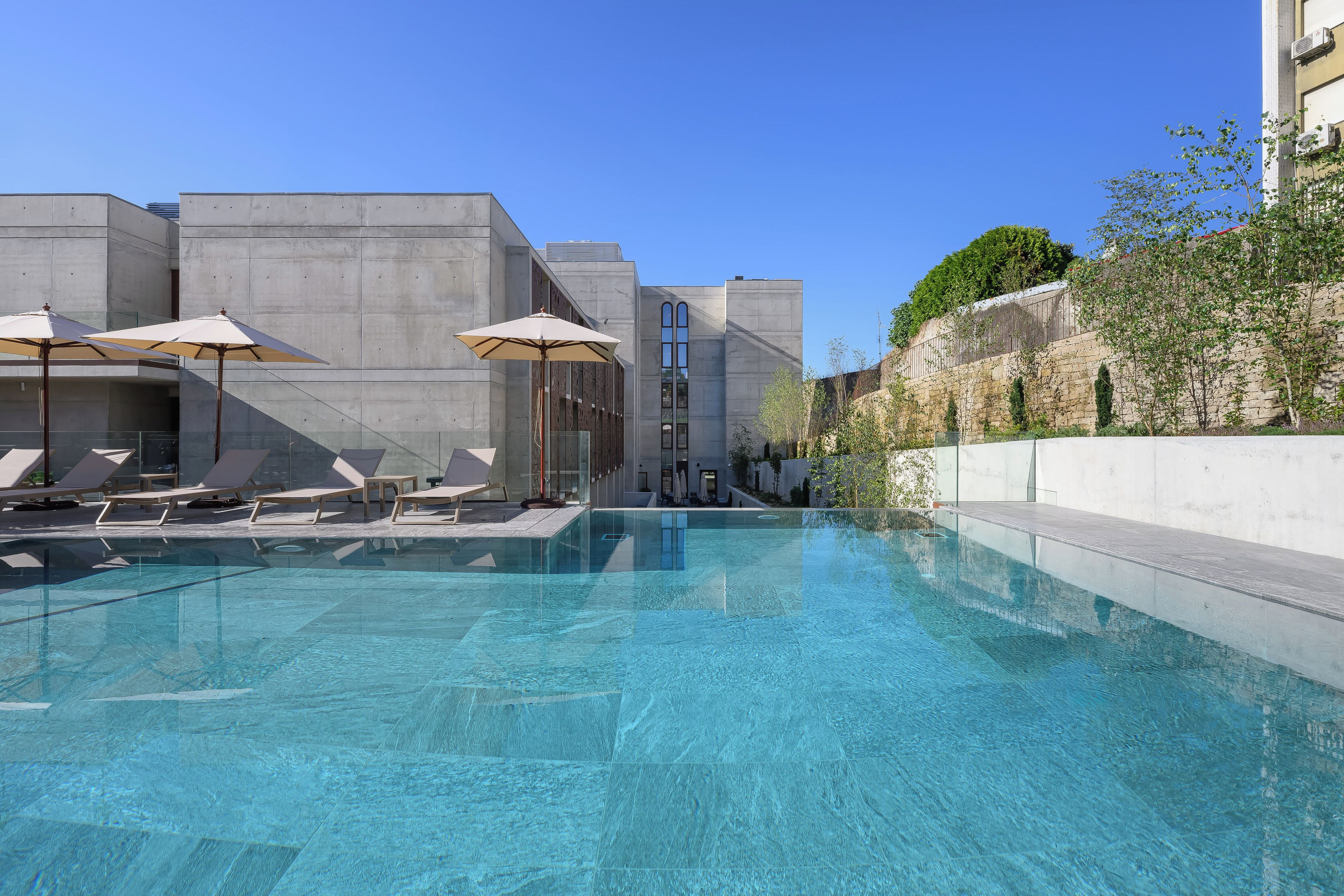 Una piscina con sillas de descanso y sombrillas, rodeada de edificios modernos.