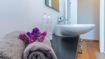 Une salle de bain avec une serviette, des fleurs violettes et des articles de toilette posés sur le comptoir.