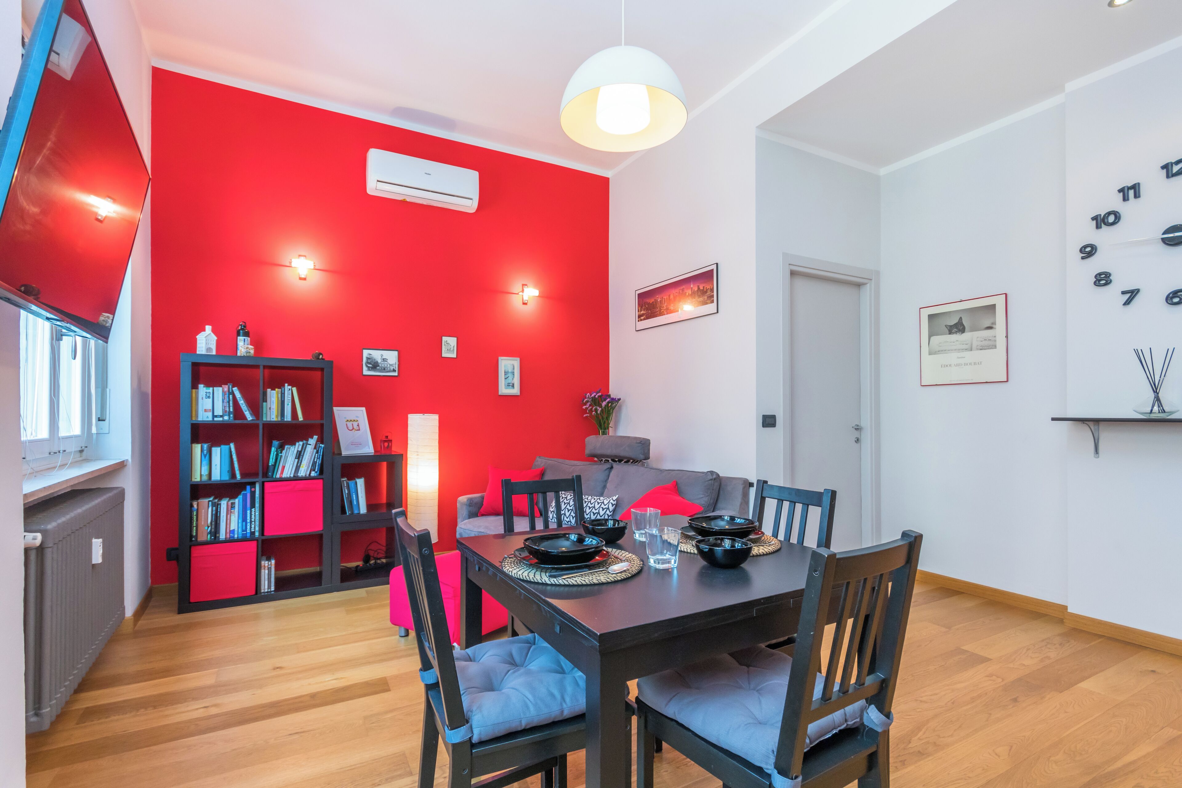 Un comedor con una pared de acento roja, una estantería y una lámpara colgante moderna.