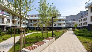 Et moderne lejlighedskompleks med en central gårdsplads, udendørs siddepladser og en belagt sti.