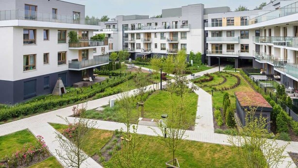 Et moderne lejlighedskompleks med flere altaner, en central gårdsplads med grønne områder og en sti for fodgængere.