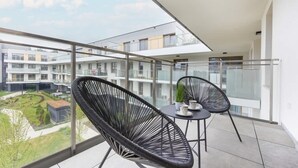 En balkon med to sorte fletstole og et lille bord, med udsigt over et boligområde med moderne bygninger.