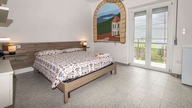 Un dormitorio con cama, mesitas de noche, un cuadro y puerta al balcón.