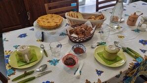 Una mesa servida con pastel, pan y aderezos, con mantel floral y platos verdes.