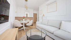 Una sala de estar moderna con un sofá blanco, una mesa de centro de vidrio y un comedor con una mesa y sillas blancas.