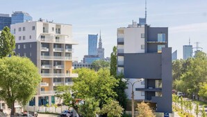 Un moderno edificio de apartamentos con varios balcones, rodeado de árboles y otros edificios urbanos.