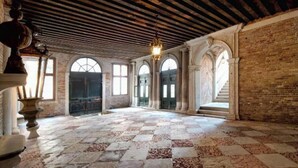 Un amplio salón con piso a cuadros, arcos y una escalera que sube a un nivel superior.