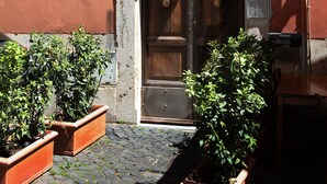 A building entrance with a wooden door, potted plants, and a sign. - Unique Trastevere (Roma)
