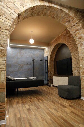 A room with a brick archway, a bed, a TV mounted on the wall, and a wooden floor. - Unique Trastevere (Roma)