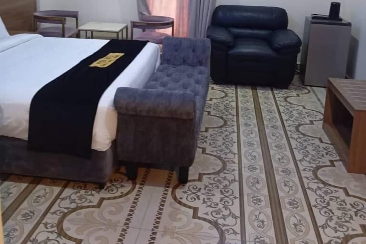 Een hotelkamer met een bed, een grijze fauteuil, een klein tafeltje, een decoratief vloerkleed en een airconditioning.