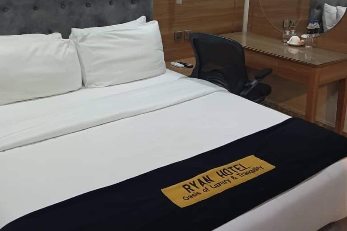 Een hotelkamer met een bed, een bureau en een stoel. Er ligt een naambordje op het bed.