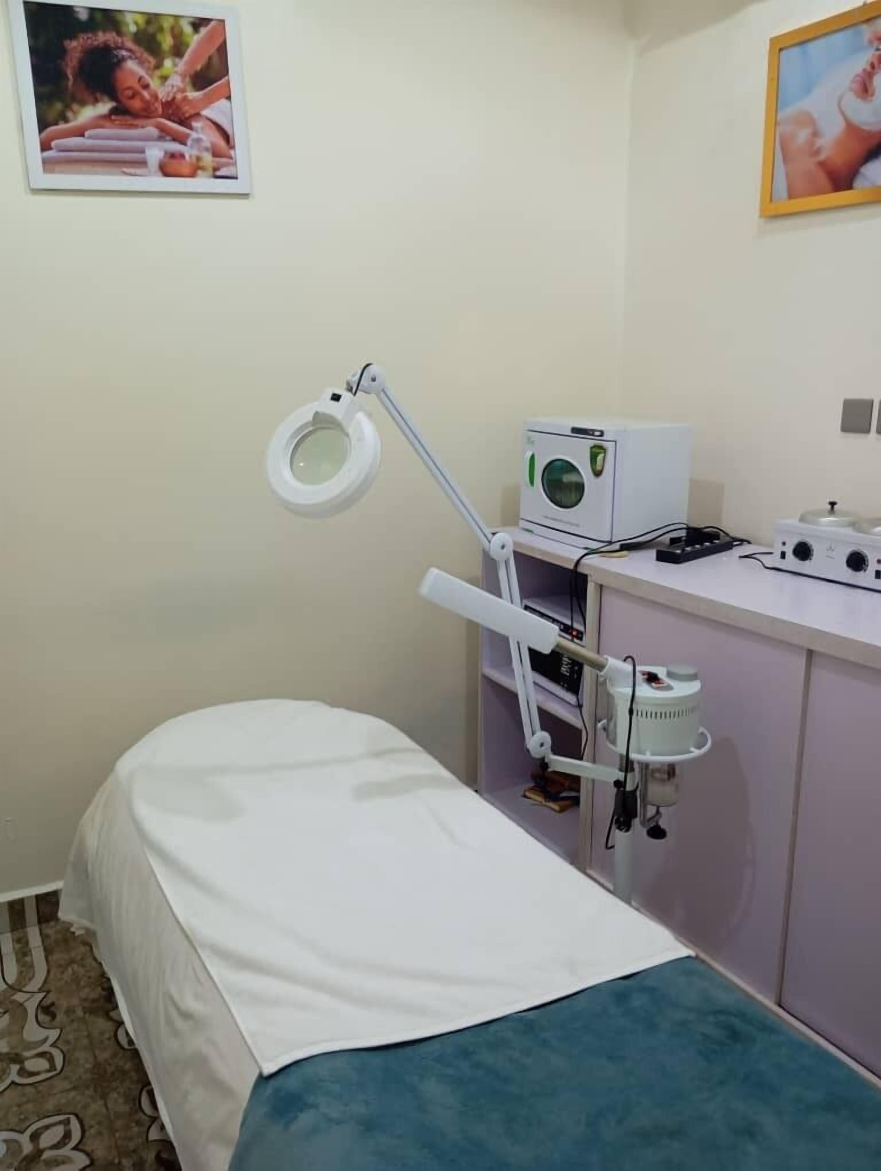 Un consultorio clínico con una cama, una lámpara médica, un esterilizador y un lavamanos.