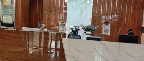Una zona de recepción con mostrador de mármol, paneles de madera y un reloj de pared.