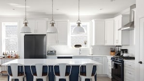 A modern kitchen with white cabinets, a central island with bar stools, a black refrigerator, a stove, and pendant lighting.