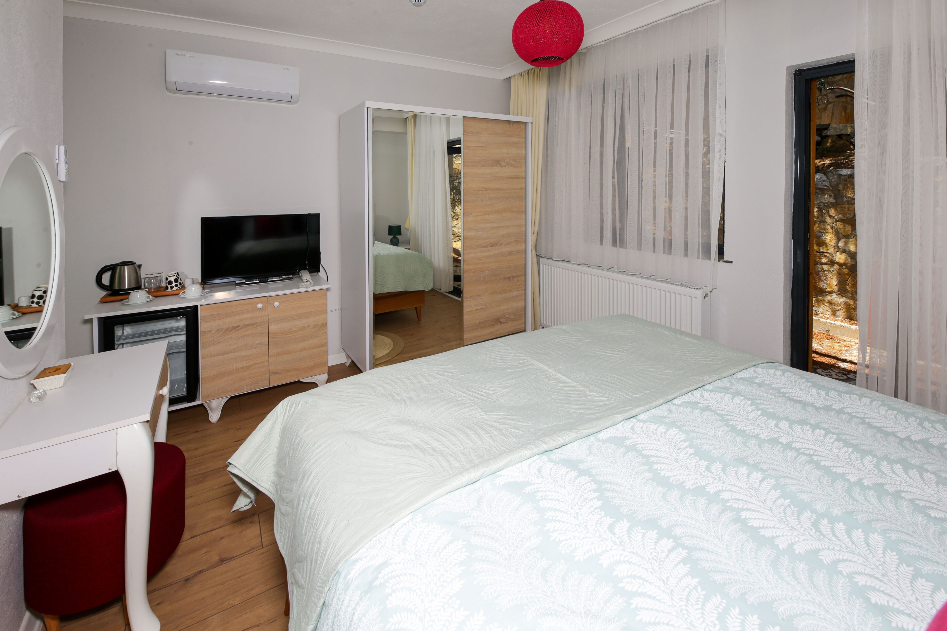 Un dormitorio con cama, televisor, escritorio, espejo y una silla roja.