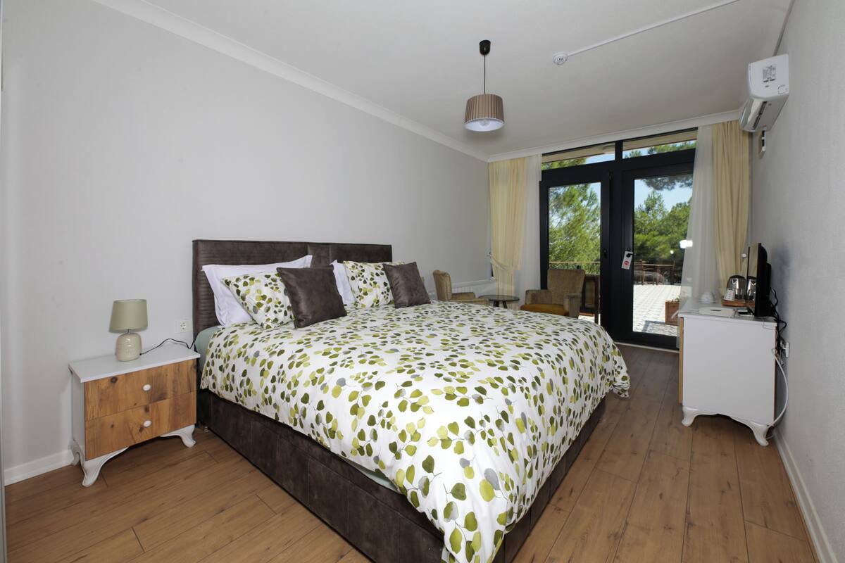 Une chambre à coucher avec un grand lit, une table de chevet, une commode et une fenêtre avec des rideaux.