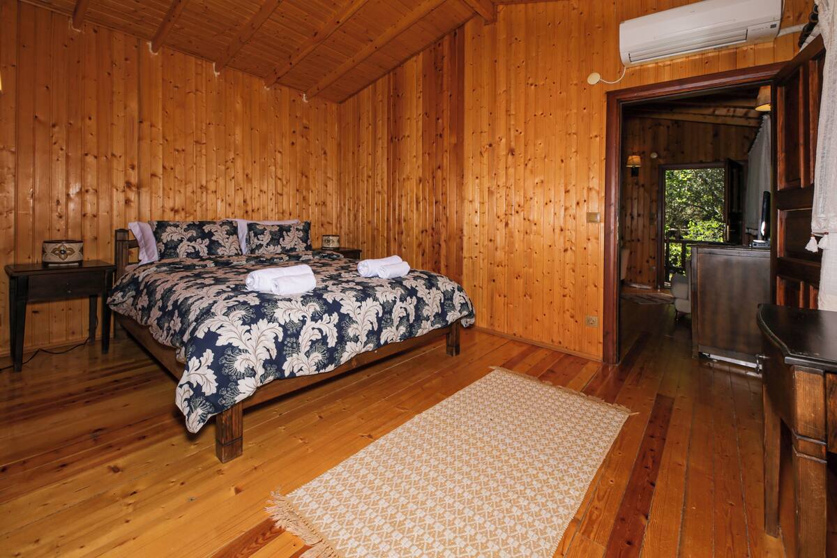 Une chambre à coucher aux murs lambrissés, comprenant un lit, une table de chevet, une commode et un appareil de climatisation.