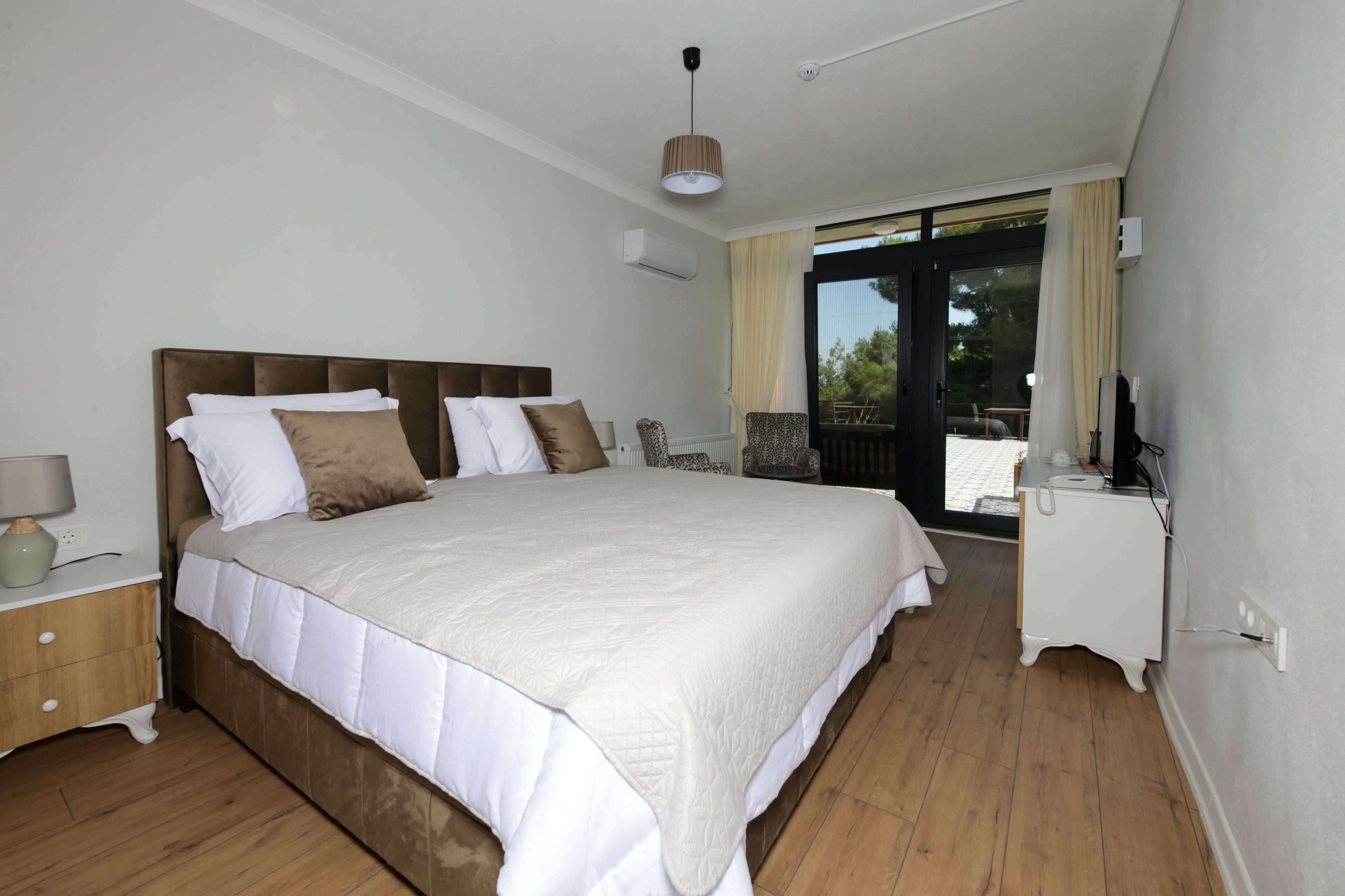 A bedroom with a large bed, a nightstand, a dresser, and a view of the outdoors through a sliding glass door.