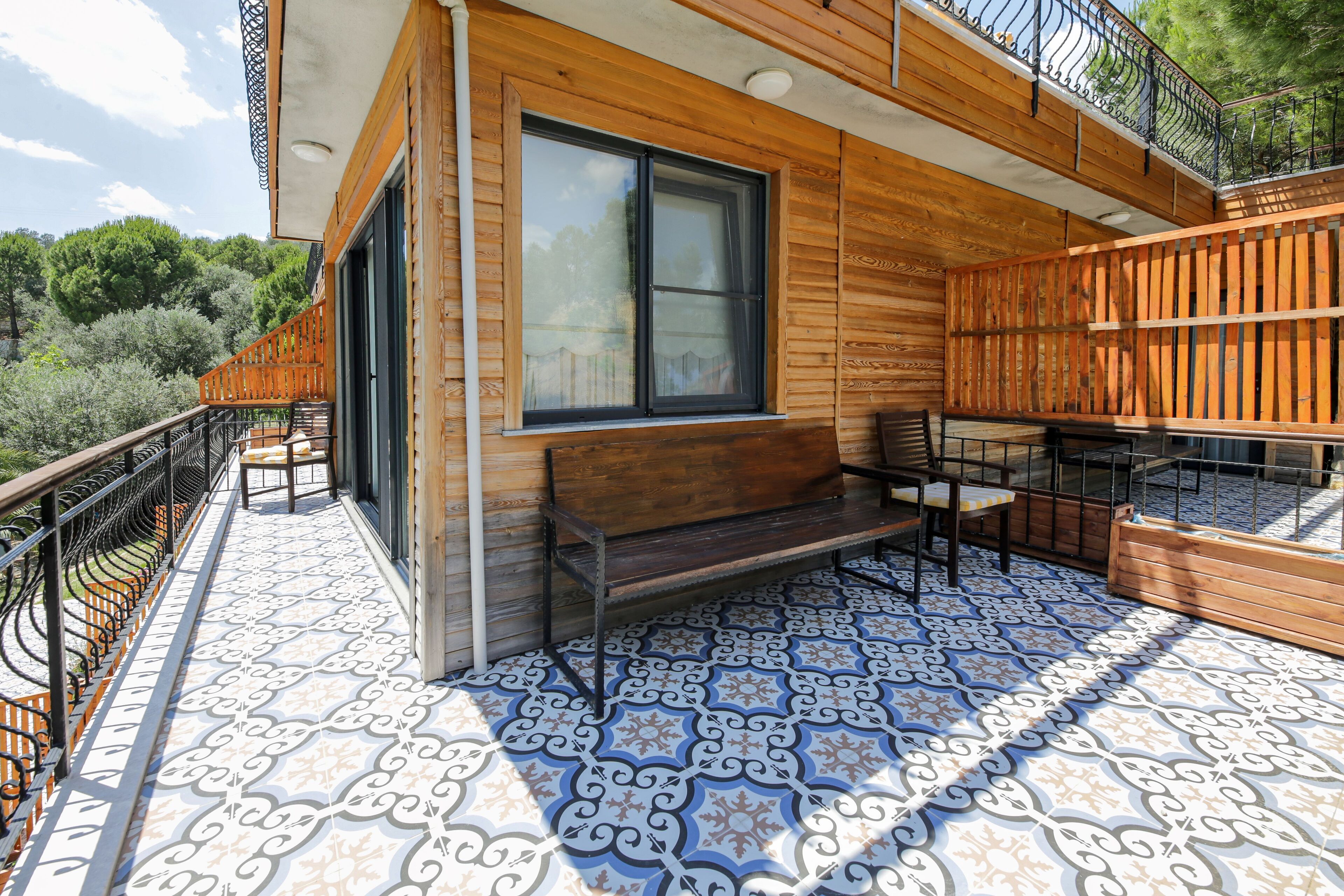 Una terraza de madera con suelo de baldosas estampadas, un banco y una mesa.