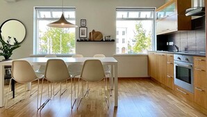 Eine moderne Küche mit Holzschränken, einem eingebauten Backofen und einem Essbereich mit einem weißen Tisch und Stühlen.