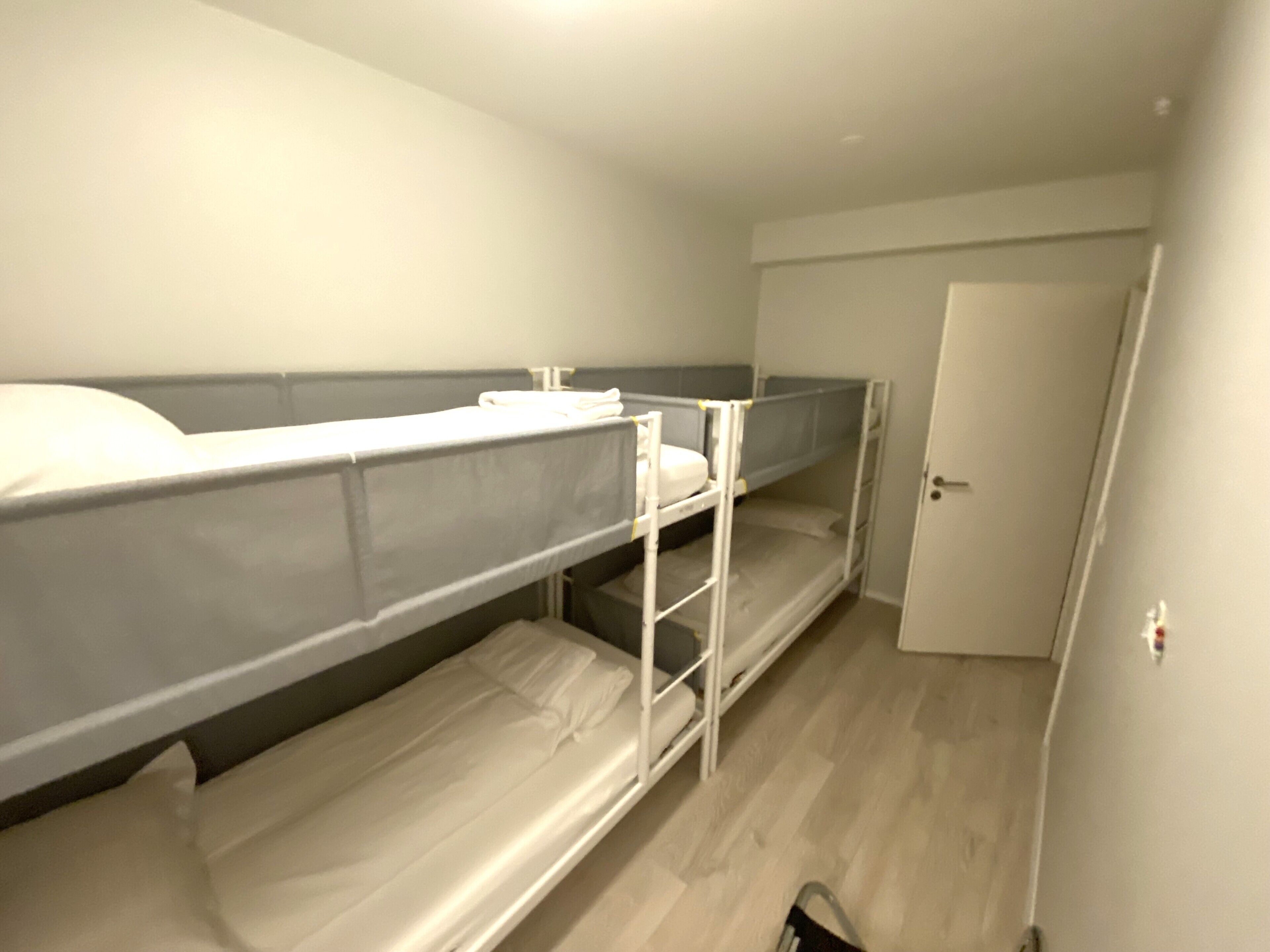 A dormitory room with bunk beds, a door, and a light switch on the wall.
