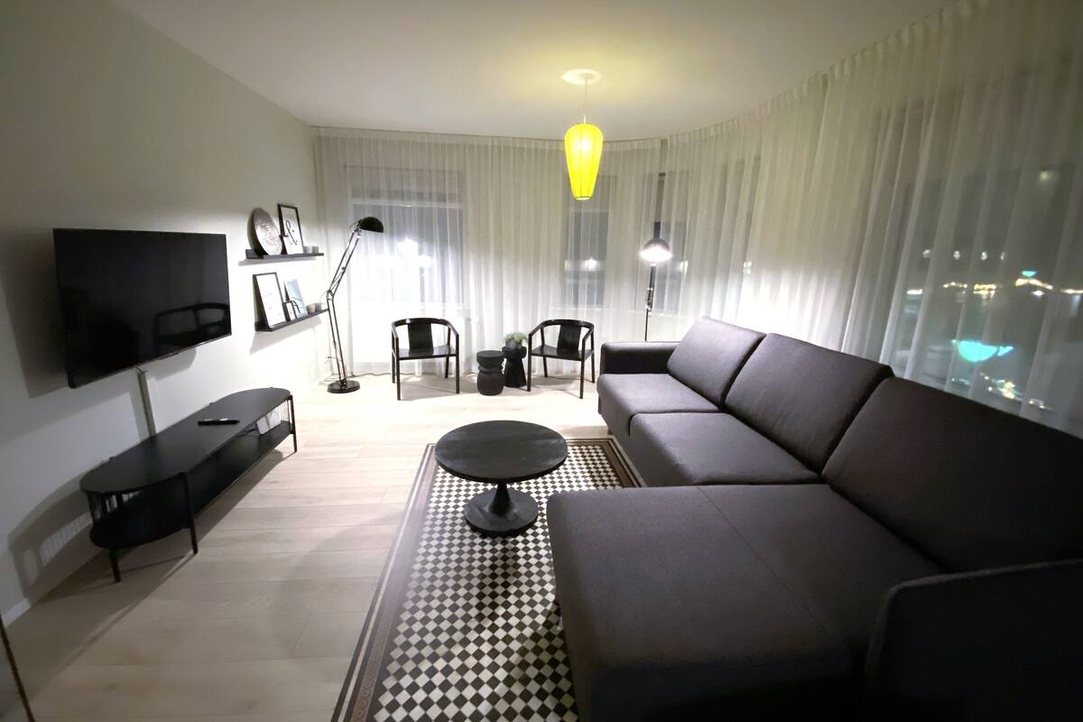 Una sala de estar moderna con un televisor de pantalla plana, un sofá, una mesa de centro y una alfombra estampada.
