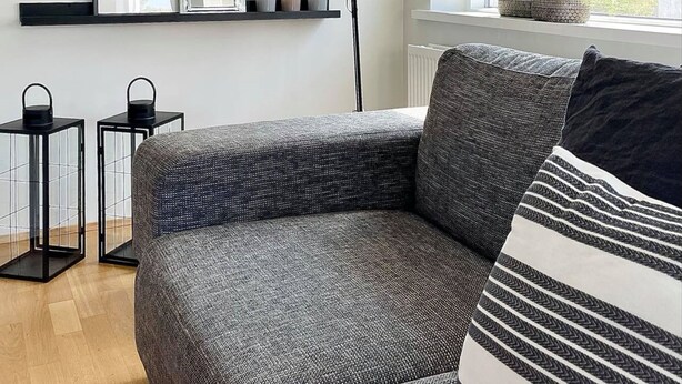 Ein modernes Wohnzimmer mit grauem Sofa, Kissen in Schwarz-Weiß-Streifen, einer schwarzen Stehlampe und einem Fenster mit Blick auf eine grüne Landschaft.