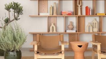 A modern interior with a wooden bookshelf, two leather chairs, a round wooden stool, and a potted plant.