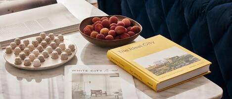 A table with a bowl of lychees, a plate of round objects, a book titled 'The Ideal City', and a magazine titled 'WHITE CITY'.